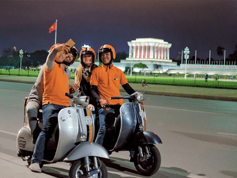Guests on the back of a vintage Vespa taking a photo with their drivers in Hanoi