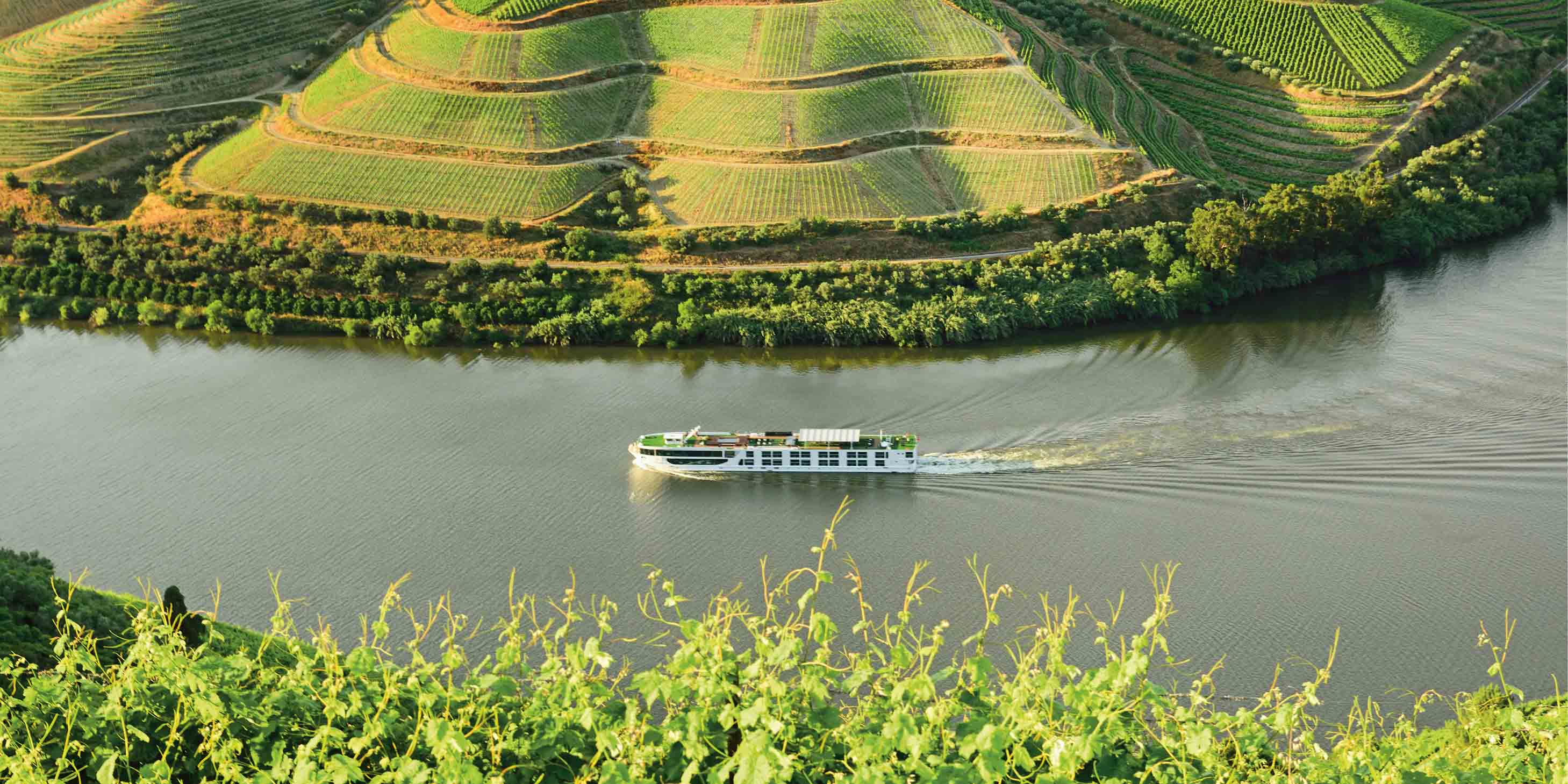 River cruise ship sailing along the bend of a river surrounded by wineries