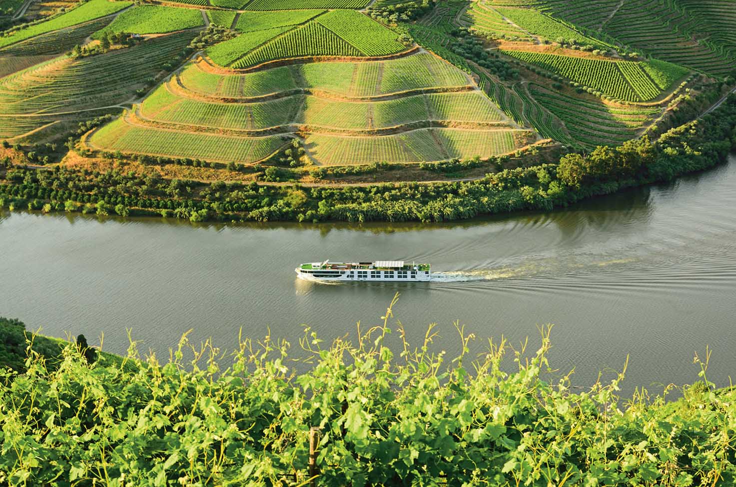 River cruise ship sailing around the bend of a river surrounded by wineries