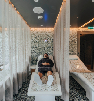 A man relaxes on a bed in a serene spa room, surrounded by calming decor and soft lighting.
