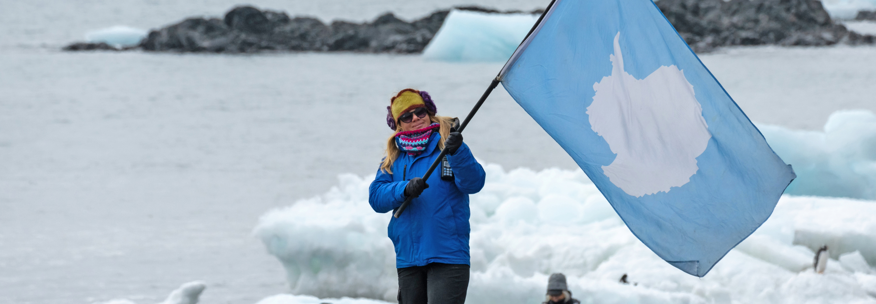 Woman waving antarctican flag with ice bergs behind