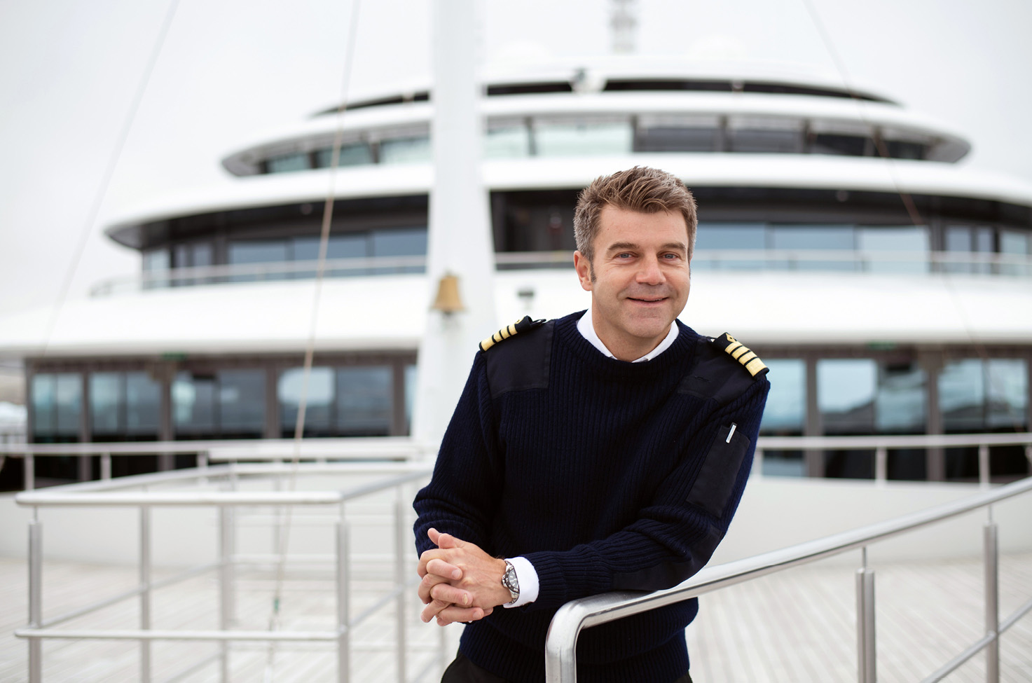 The Scenic Eclipse captain stands on the deck of the ship smiling and wearing a dark jumper
