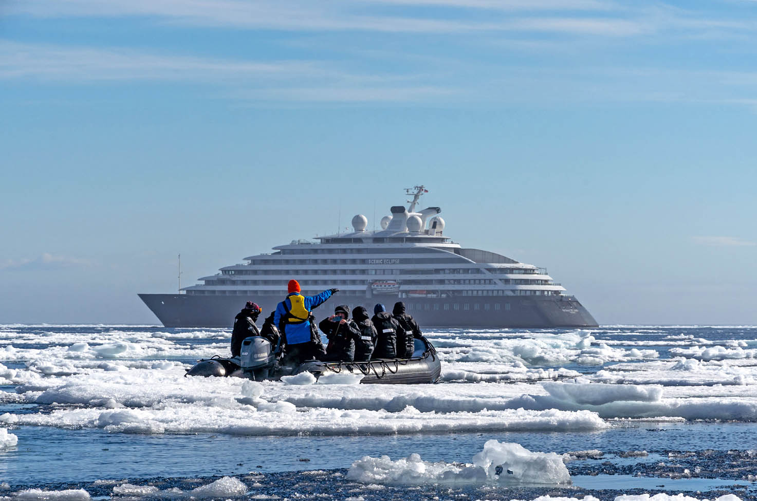 A group of guests with a guide on board a Zodiak boat, with ice floating in the sea and Scenic Eclipse in the background