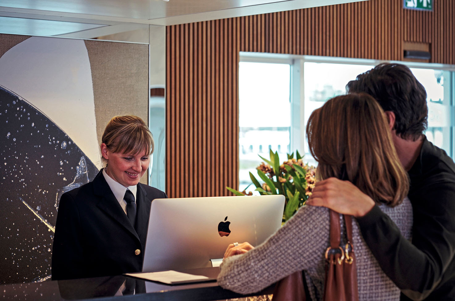 A couple checking in on their cruise ship with a member of the crew on reception looking at a screen